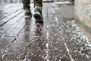 Person walking along paver walkway with ice melt pellets spread across the top, during winter