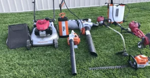 Lawn equipment, such as mower, blower, trimmer, and edger, are resting on top of a lush, green lawn